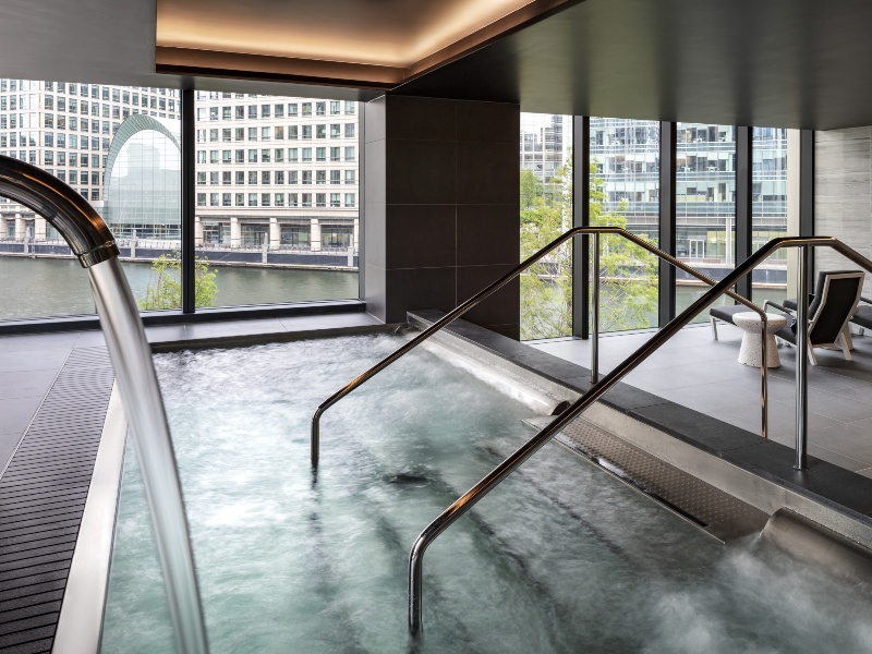 Interior photo of swimming pool and steps, with large glass windows giving views over the Canary Wharf area