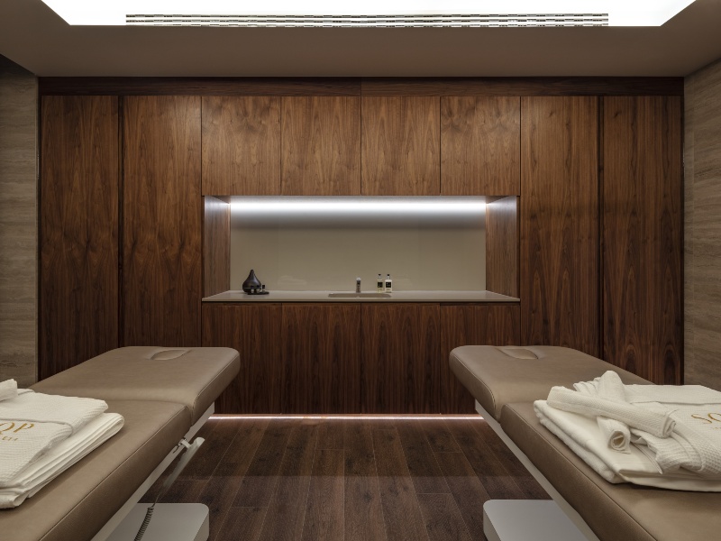 Interior photo of a spa area, with wood panelled walls and floors with 2 benches with towels
