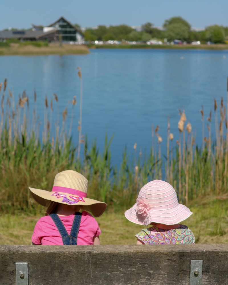 Two children wearing hats, sitting on a bench in front of Stanwick lake