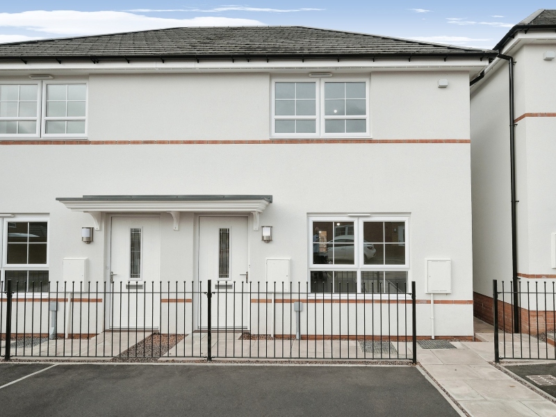 Exterior photo of an actual three bedroom Shared Ownership house at Lower, Lane, Coleford,. Exterior rendered in white, with railings in front of car parking space