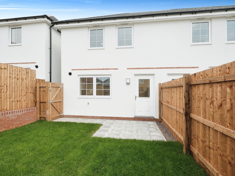 Exterior photo of an actual three bedroom Shared Ownership house at Lower, Lane, Coleford,. Exterior rendered in white, with patio paving , leading to turfed lawn, with wooden fencing border