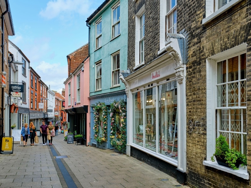 View along the traditional paved Lower Goat Lane shops, with large window displays colourful blue walls and flowers