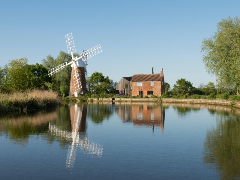 View across the Norfolk Broads , looking across the water with old fashioned windmill and mill house on the waterfront