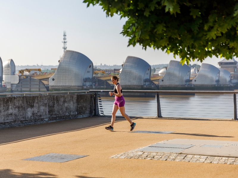 Exterior photo of a man jogging in Barrier Park, with the Thames Barrier in the background