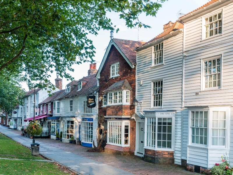 Photo of a row of 15th-18th Century buildings, houses and shops, along the High Street. Brick house is Quill House, others are white wooden clapboarded houses in Tenterden, Kent