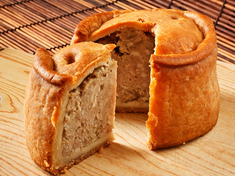 A traditional handmade pork pie, a slice cut out, traditionally called Melton Pies from the town of Melton Mowbray in the Midlands, England