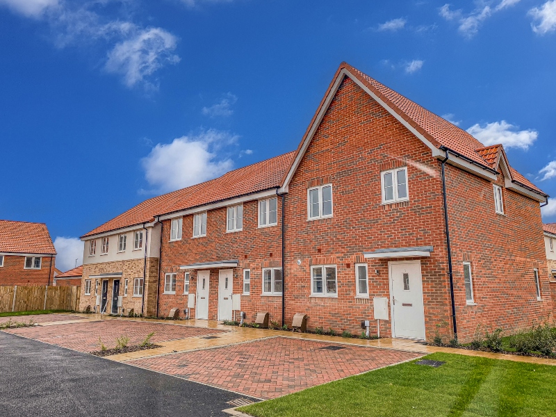 Exterior view of a terrace of homes at Sorrel Grove, Norfolk, with parking spaces and lawn outside