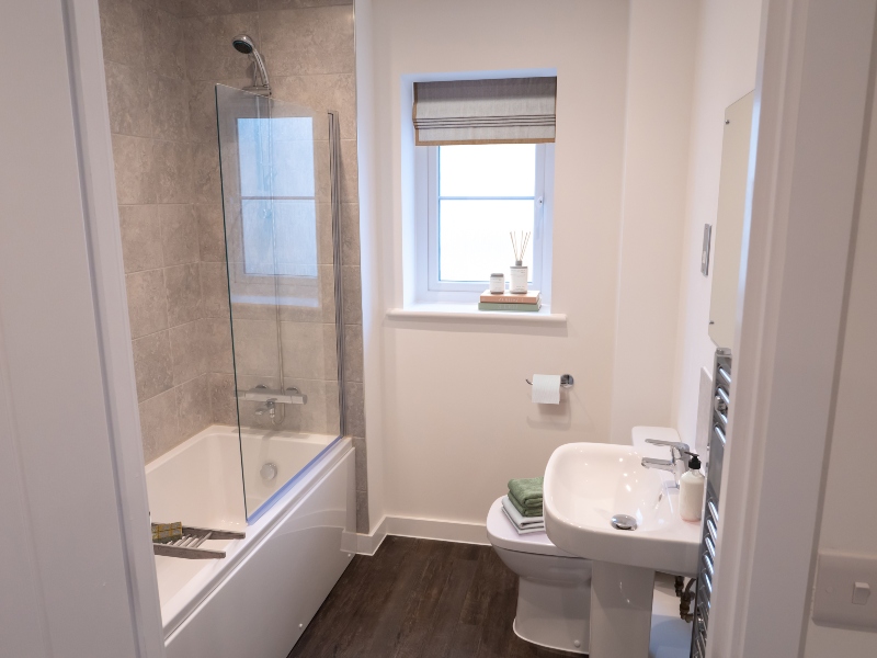 Interior view of a CGI dressed bathroom taken in an actual 3 bed bungalow at Benson Grange, showing bath with glass screen, handbasin and toilet and single window