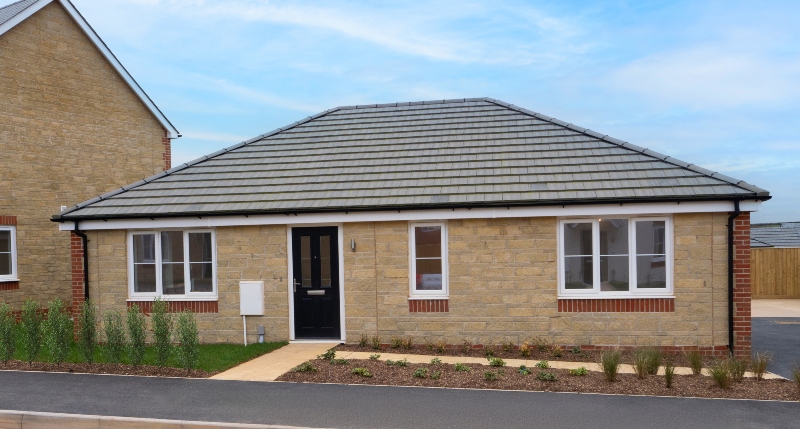 Exterior frontal view of a finished, 1 storey 3 bedroom bungalow at Benson Grange, stone clad front with shrub border and path in front