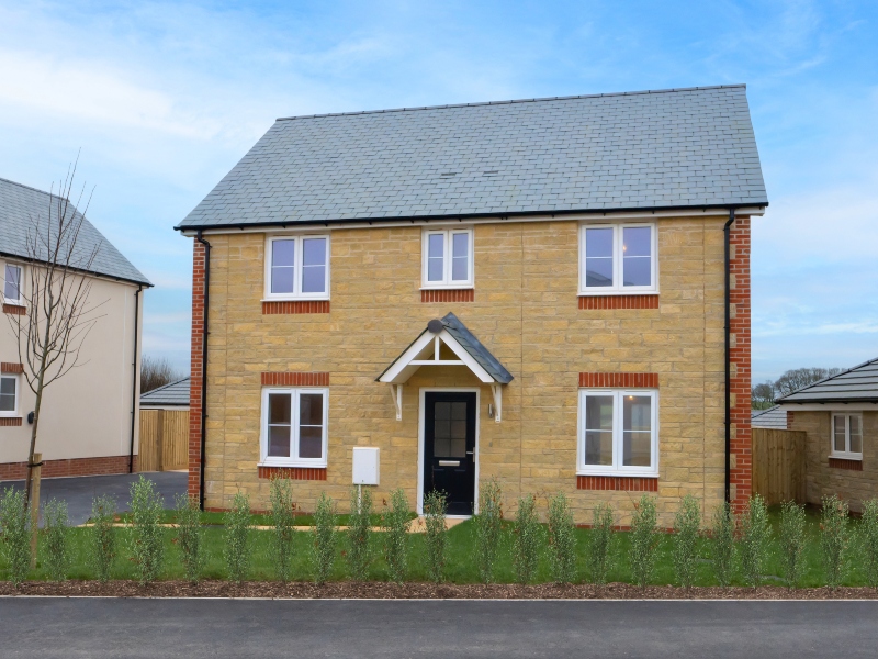 Exterior frontal view of a finished, 2 storey 4 bedroom house at Benson Grange, stone clad front with shrub border and path in front