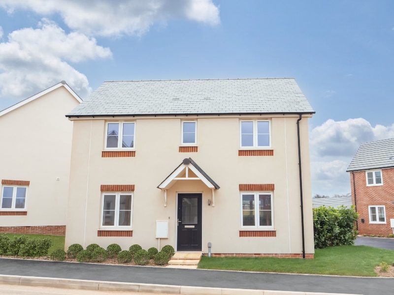 Exterior frontal view of a finished, 2 storey 3 bedroom house at Benson Grange, cream renderef front with shrub border and path in front