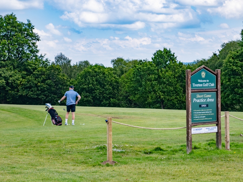 Man with golf bag standing on a green at Tiverton Golf club with the Golf Club sign in the foreground