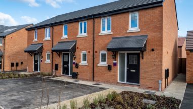 Front exterior view of a terrace of 3 two bed houses taken at Millbrook Place, Crewe, showing front doors, parking spaces and planting outside.