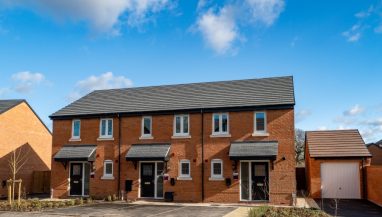 Front exterior view of a terrace of 3 two bed houses taken at Millbrook Place, Crewe, showing front doors, parking spaces and planting outside.