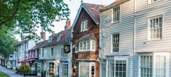 Photo of a row of 15th-18th Century buildings, houses and shops, along the High Street. Brick house is Quill House, others are white wooden clapboarded houses in Tenterden, Kent