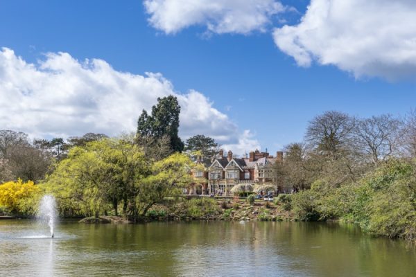 A view across the lake of Bletchley Park Manor, the home of code breaking in WW2, surround by tress with no leaves on a sunny winter day.