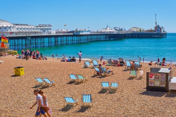 Brighton beach with people enjoying the sunshine and the Brighton Pier in the background.