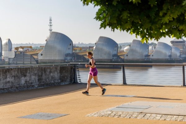 Exterior photo of a man jogging in Barrier Park, with the Thames Barrier in the background